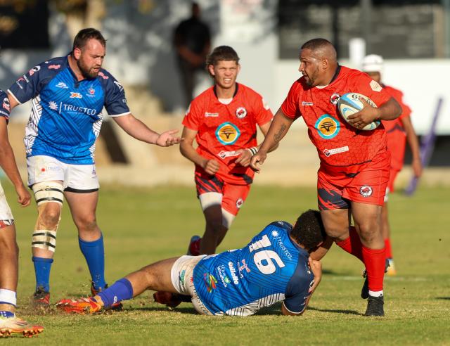 WINDHOEK, 18 July 2026 - Miquel Busch of Rehoboth (in red) with the ball resists Gerhard Oppermann (in blue on the ground) of Trustco United during round eight of the Namibia Rugby Union Premier League at the Trustco United field in Olympia. (Photo by: Hesron Kapanga) NAMPA