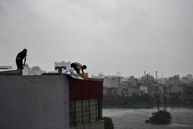 Two men try to fix a damaged roof as heavy rains and high winds from Typhoon Yagi impact Hai Phong on September 7, 2024. Typhoon Yagi was set to slam into Vietnam on September 7 after impacting southern China, on course to hit the northern and north-central regions around the famed UNESCO heritage site Halong Bay. (Photo by NHAC NGUYEN / AFP)