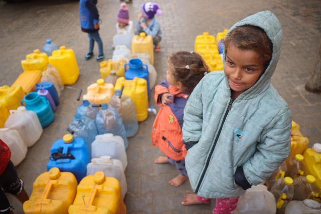 Barefoot Palestinian girls queue near their containers to resupply with water at a makeshift displacement encampment at the Bureij refugee camp in the central Gaza Strip on November 24, 2024, amid the ongoing war between Israel and the Palestinian Hamas militant group. (Photo by Eyad BABA / AFP)