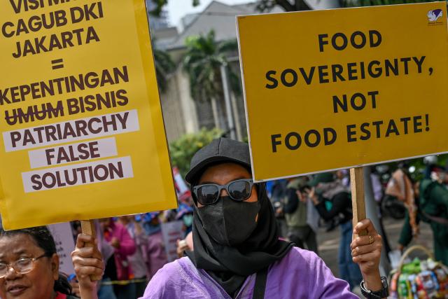 An activist holds placards against the patriarchy and food security during a street protest on the International Day for the Elimination of Violence Against Women, in Jakarta on November 25, 2024. (Photo by BAY ISMOYO / AFP)