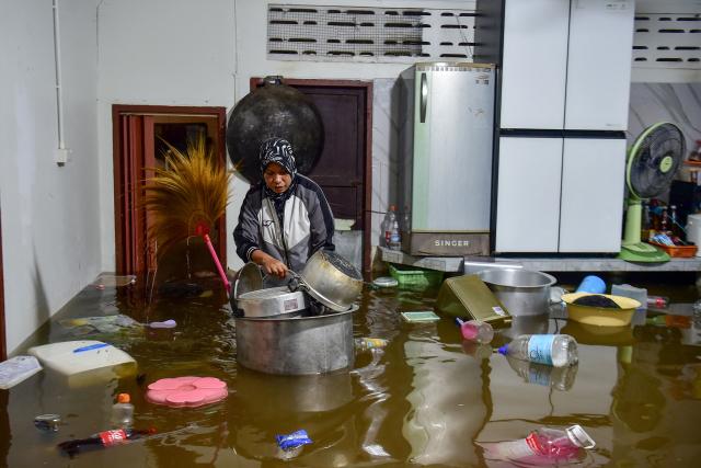 (FILES) A resident looks through belongings floating in flood waters inside her home following heavy rain in Thailand's southern province of Narathiwat on November 28, 2024. Flooding driven by heavy rains in southern Thailand has killed nine people and displaced more than 13,000, officials said November 30, as rescue teams using boats and jet skis worked to reach stranded residents. (Photo by Madaree TOHLALA / AFP)