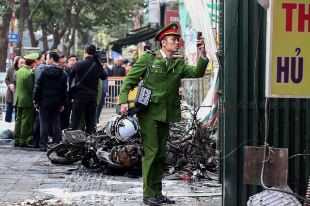 A police officer takes a photo outside the scene of a fire at a karaoke bar in Hanoi on December 19, 2024. A fire that ripped through a karaoke bar in the Vietnamese capital killed 11 people and injured two others in a suspected arson attack, police said on December 19. (Photo by Nam NGUYEN / AFP)