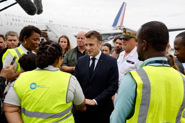 France's President Emmanuel Macron (C) speaks with staff members as he arrives on the tarmac of Dzaoudzi's airport, on the French Indian Ocean territory of Mayotte, on December 19, 2024, following the cyclone Chido's passage over the archipelago. French President Emmanuel Macron on December 19, 2024, arrived in Mayotte to assess the devastation wrought by Cyclone Chido on the Indian Ocean archipelago, as rescuers raced to search for survivors, an AFP journalist said. Macron's plane landed at 10:10 am local time (0710 GMT) with some twenty doctors, nurses and civil security personnel on board, as well as four tonnes of food and sanitary supplies. (Photo by Ludovic MARIN / POOL / AFP)