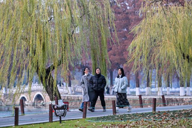 People walk along the East Lake in Wuhan in China's central Hubei province on December 21, 2024, ahead of the fifth anniversary of China confirming its first death from the Covid-19 coronavirus. (Photo by HECTOR RETAMAL / AFP)