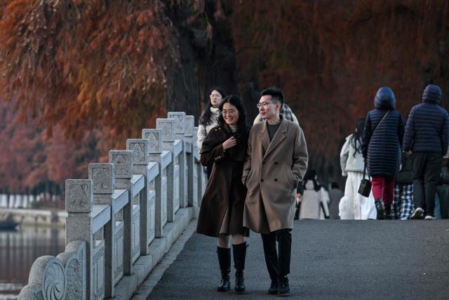 People walk along the East Lake in Wuhan in China's central Hubei province on December 21, 2024, ahead of the fifth anniversary of China confirming its first death from the Covid-19 coronavirus. (Photo by HECTOR RETAMAL / AFP)