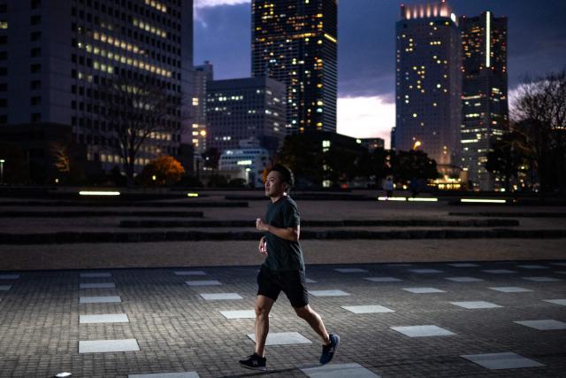 A man runs as the city's skyline is seen at dusk in Yokohama on December 21, 2024. (Photo by Philip FONG / AFP)