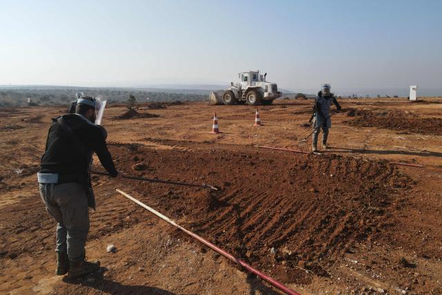 An aerial view shows members of the HALO Trust NGO working on clearing mines from a field in the town of Musibin in Syria's Idlib province on December 19, 2024. Islamist-led rebels took Damascus in a lightning offensive on December 8, ousting president Bashar al-Assad and ending five decades of Baath rule in Syria. (Photo by MUHAMMAD HAJ KADOUR / AFP)