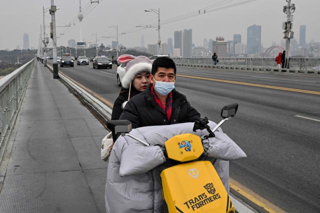 A couple rides a scooter on the Wuhan bridge over the Yangtze river in Wuhan, in China's central Hubei province on December 22, 2024, ahead of the fifth anniversary of China confirming its first death from the Covid-19 coronavirus. (Photo by HECTOR RETAMAL / AFP)