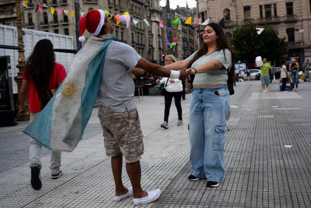 A man wearing an Argentinian flag and a Santa Claus hat dances with a woman as both take part in a Christmas solidarity dinner called 'No Families Without Christmas' in front of the National Congress in Buenos Aires on December 24, 2024. A Christmas solidarity dinner for the homeless gathered in Buenos Aires some three thousand people in front of the National Congress when poverty reaches more than half of the Argentine population after the first year of Javier Milei's ultra-liberal government. (Photo by TOMAS CUESTA / AFP)