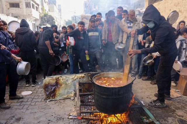 A volunteer stirs a food pot as Palestinians wait to collect humanitarian aid portions, in al-Shati camp near Gaza City on December 26, 2024, amid the ongoing war between Israel and the Palestinian Hamas movement. (Photo by Omar AL-QATTAA / AFP)