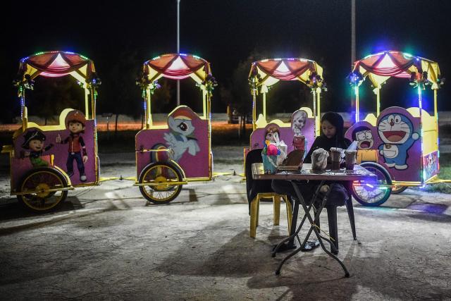 A vendor uses mobile phone as she waits for customers at Pantai Batu Buruk in Kuala Terengganu on December 26, 2024. (Photo by ARIF KARTONO / AFP)