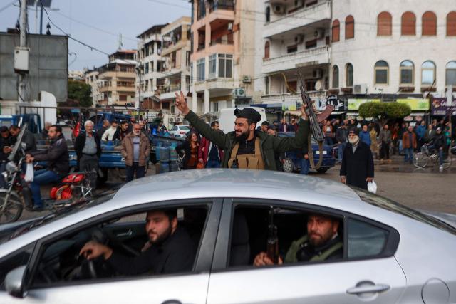 A fighter affiliated with Syria's new administration flashes the V for victory sign in Syria's western coastal city of Latakia on December 26, 2024. Syria's new authorities launched an operation in a stronghold of ousted president Bashar al-Assad on December 26, with a war monitor saying three gunmen affiliated with the former government were killed, a day after angry protests erupted in several areas around Syria over a video showing an attack on an Alawite shrine that circulated online. (Photo by AAREF WATAD / AFP)