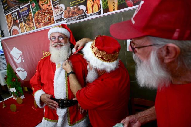 Limachem Cherem (C), director of Brazil's Santa Claus School, cuts the beard of a Santa Claus during an annual event called "Barbas de Molho" (Beards at Rest) at a restaurant in Rio de Janeiro, Brazil, on December 26, 2024. The meeting is a tradition of the group to celebrate the end of the Christmas season. (Photo by Mauro PIMENTEL / AFP)