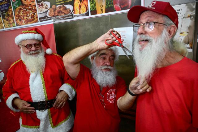 Limachem Cherem (C), director of Brazil's Santa Claus School, cuts the beard of a Santa Claus during an annual event called "Barbas de Molho" (Beards at Rest) at a restaurant in Rio de Janeiro, Brazil, on December 26, 2024. The meeting is a tradition of the group to celebrate the end of the Christmas season. (Photo by Mauro PIMENTEL / AFP)