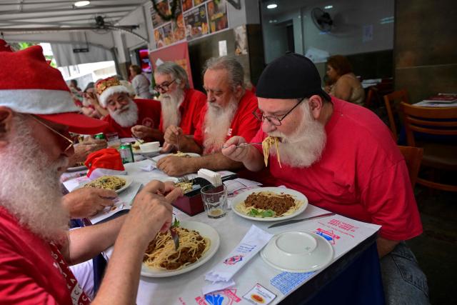 A group of professional Santas from Brazil's Santa Claus School has lunch during an annual event called "Barbas de Molho" (Beards at Rest) at a restaurant in Rio de Janeiro, Brazil, on December 26, 2024. The meeting is a tradition of the group to celebrate the end of the Christmas season. (Photo by Mauro PIMENTEL / AFP)