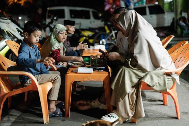 People eat in front of a food stall on a street in Banda Aceh on December 26, 2024. (Photo by Yasuyoshi CHIBA / AFP)