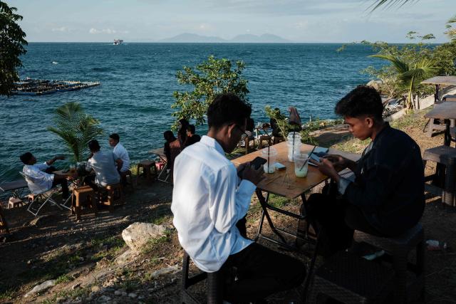 People spend time by the seaside during sunset in Banda Aceh on December 26, 2024.  (Photo by Yasuyoshi CHIBA / AFP)