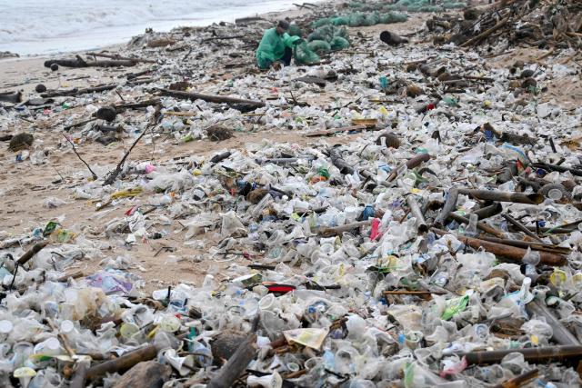 A man collects plastic and other debris washed ashore at a beach in Kedonganan, Badung Regency, on Indonesia's resort island of Bali on December 27, 2024. (Photo by SONNY TUMBELAKA / AFP)