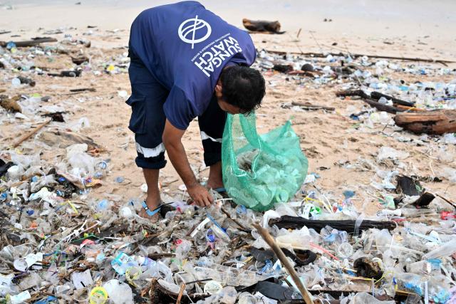 A man collects plastics and other debris washed ashore at a beach in Kedonganan, Badung Regency, on Indonesia's resort island of Bali on December 27, 2024. (Photo by SONNY TUMBELAKA / AFP)