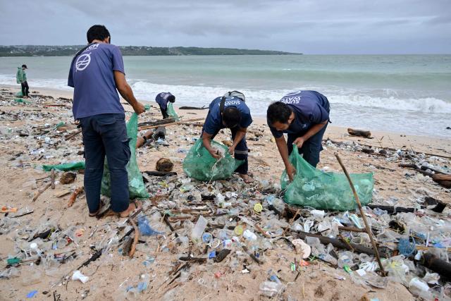 People collect plastic and other debris washed ashore at a beach in Kedonganan, Badung Regency, on Indonesia's resort island of Bali on December 27, 2024. (Photo by SONNY TUMBELAKA / AFP)