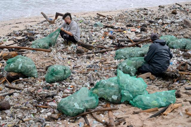 People collect plastic and other debris washed ashore at a beach in Kedonganan, Badung Regency, on Indonesia's resort island of Bali on December 27, 2024. (Photo by SONNY TUMBELAKA / AFP)