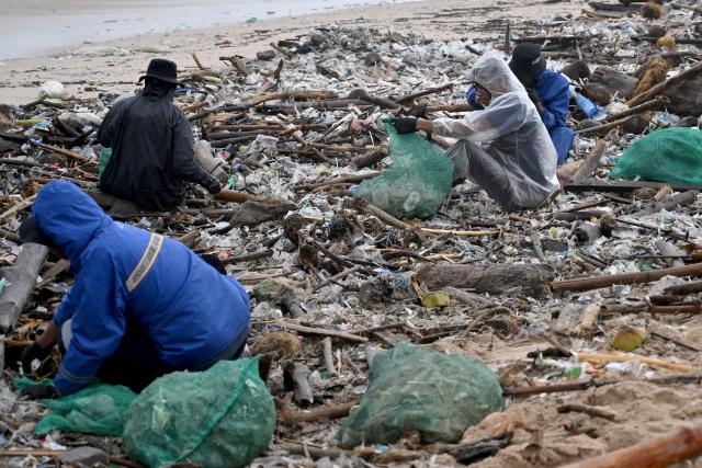 People collect plastic and other debris washed ashore at a beach in Kedonganan, Badung Regency, on Indonesia's resort island of Bali on December 27, 2024. (Photo by SONNY TUMBELAKA / AFP)