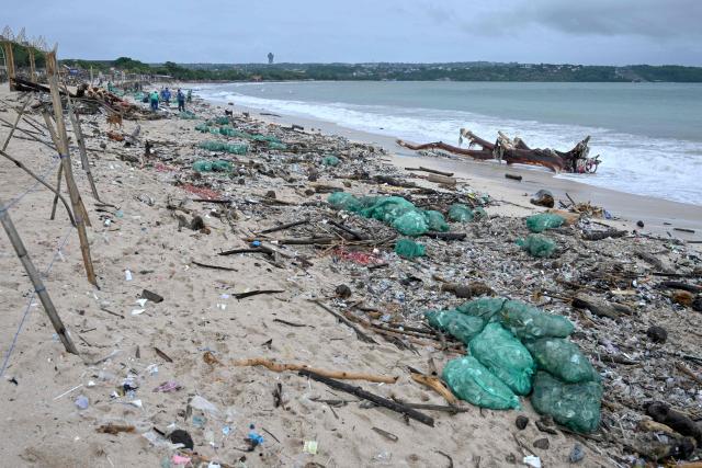 People collect plastic and other debris washed ashore at a beach in Kedonganan, Badung Regency, on Indonesia's resort island of Bali on December 27, 2024. (Photo by SONNY TUMBELAKA / AFP)