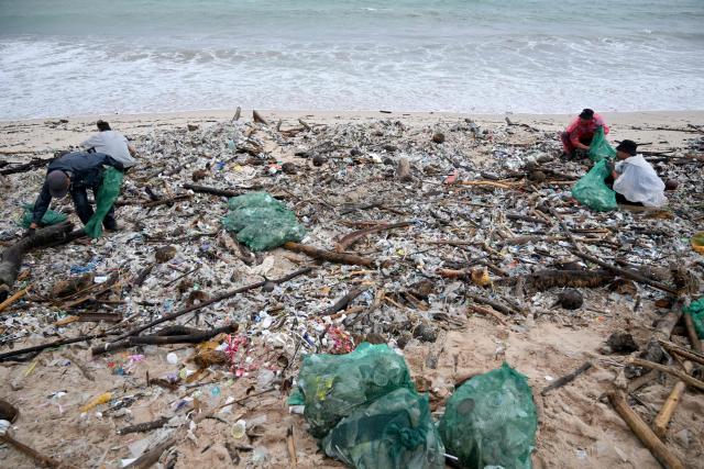 People collect plastic and other debris washed ashore at a beach in Kedonganan, Badung Regency, on Indonesia's resort island of Bali on December 27, 2024. (Photo by SONNY TUMBELAKA / AFP)