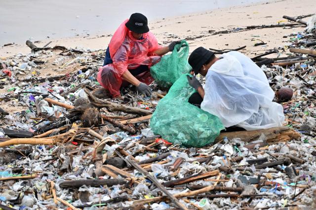 People collect plastic and other debris washed ashore at a beach in Kedonganan, Badung Regency, on Indonesia's resort island of Bali on December 27, 2024. (Photo by SONNY TUMBELAKA / AFP)