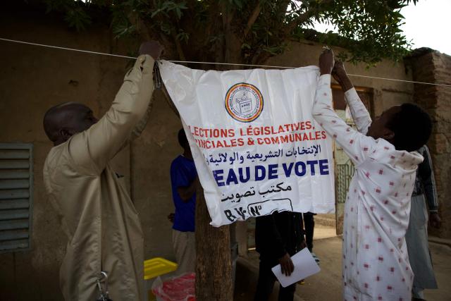 TOPSHOT - Polling station officials display a banner at a polling station in N'Djamena on December 29, 2024 at the beginnning of the local, provincial and legislative elections. Chad goes to the polls Sunday for legislative, provincial and local elections that are presented by the government as the last stage of a political transition after three years of military rule, but are being boycotted by the opposition. The boycott leaves the field open to candidates aligned with Marshal Mahamat Idriss Itno, who was brought to power by the military in 2021 and then legitimised in a presidential election last May that opposition candidates denounced as fraudulent. (Photo by Joris Bolomey / AFP)