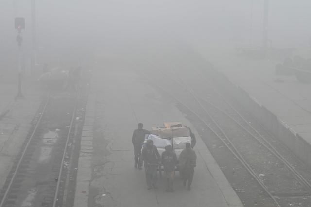 Workers carry goods at a railway station engulfed in dense fog on a cold winter morning in Lahore on December 29, 2024. (Photo by Arif ALI / AFP)