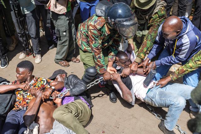 Anti-riot police attempt to break up and arrest protesters braced on the ground in a stand off during protests to demand the release of those allegedly abducted by state security agencies in Nairobi on December 30, 2024. Security forces in the East African nation have been accused of carrying out dozens of illegal detentions since youth-led anti-government demonstrations in June and July. Kenyan President William Ruto has promised an end to abductions, following the latest spate of disappearances that have been condemned by rights groups, lawyers and politicians. (Photo by Tony KARUMBA / AFP)