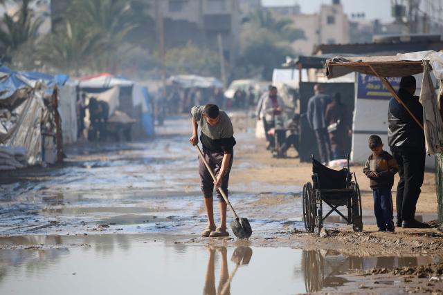 A man uses a shovel in a flood area at an internally displaced peoples' camp in Deir el-Balah in the central Gaza Strip on December 30, 2024, amid the ongoing war in the Palestinian territory between Israel and Hamas. (Photo by Eyad BABA / AFP)