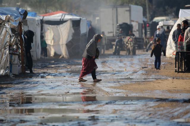 A woman crosses a flooded road following heavy rain at an internally displaced peoples' camp in Deir el-Balah in the central Gaza Strip on December 30, 2024, amid the ongoing war in the Palestinian territory between Israel and Hamas. (Photo by Eyad BABA / AFP)