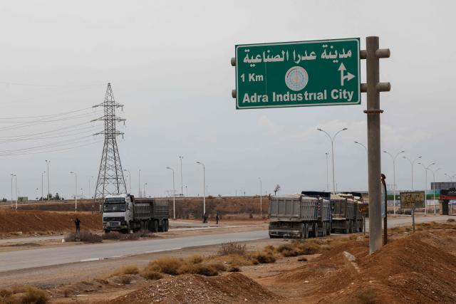 EDITORS NOTE: Graphic content / Trucks are parked near the site of an explosion at a weapons depot the previous day at the Industrial area of Adra, some 30 kilometres from the Syrian capital Damascus on December 30, 2024. An official from a nearby area, requesting anonymity, told AFP on December 29 that "an explosion of unknown origin" rocked the Adra industrial area, reporting an unspecified number of casualties and adding that rescue operations were ongoing. (Photo by ANWAR AMRO / AFP)