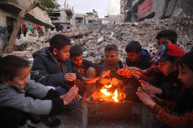 Children warm by the fire at the Bureij camp for displaced Palestinians on December 30, 2024, amid the continuing war between Israel and the militant Hamas group. Since the war between Israel and Hamas began in October last year, Gaza's 2.4 million residents have endured severe shortages of electricity, drinkable water, food and medical services. (Photo by Eyad BABA / AFP)