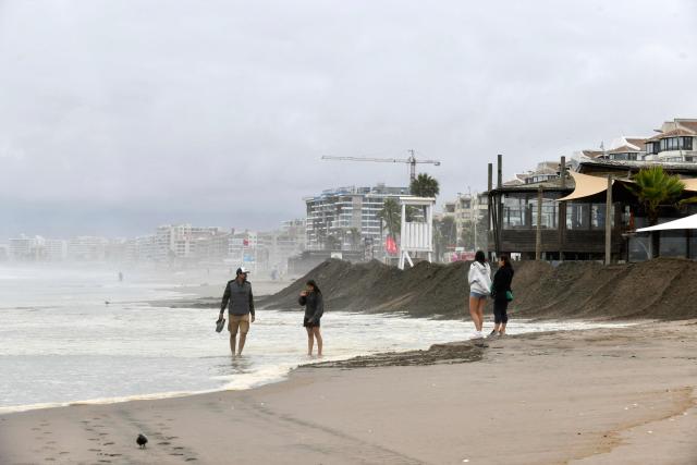 People walk on the beach after strong waves battered the coast in La Serena, Chile, on December 30, 2024. Three deaths, one in Chile, have been blamed on large waves up to 13 feet (four metres) pummelling Ecuador, Chile and Peru, where nearly 100 ports have been closed because of the rough conditions. The phenomenon began on Christmas and is expected to last until January 1, according to Peru's National Emergency Operations Center. (Photo by Alejandro PIZARRO / AFP)