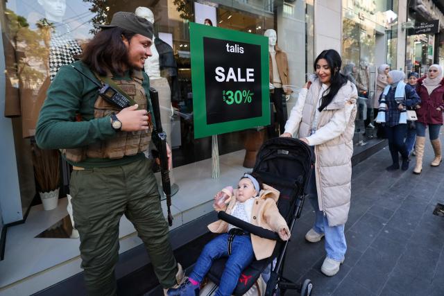 A fighter affiliated with Syria's new administration chats with a woman on the street the al-Shalaan area in central Damascus on January 2, 2025. (Photo by ANWAR AMRO / AFP)