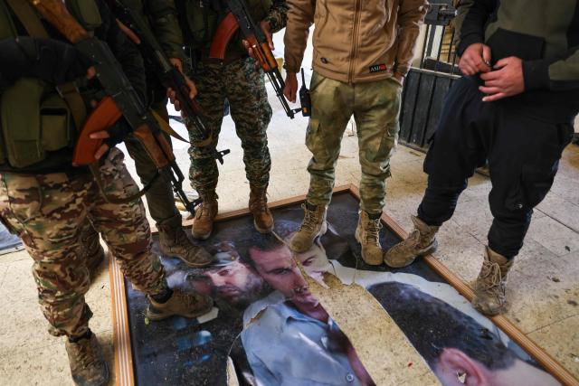 Fighters affiliated with Syria's new administration pose for a picture as they stand on a damaged portrait of deposed president Bashar al-Assad inside the defunct Mezzeh military prison in Damascus on January 2, 2025. (Photo by ANWAR AMRO / AFP)