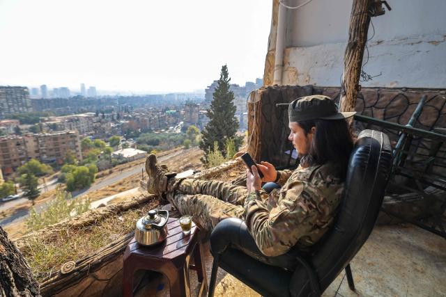 A fighters affiliated with Syria's new administration checks his phone as he sits outside the defunct Mezzeh military prison overlooking the capital Damascus on January 2, 2025. (Photo by ANWAR AMRO / AFP)