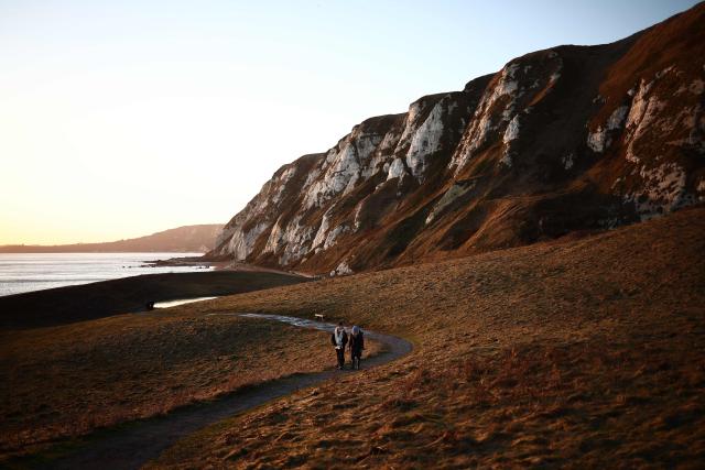 People walk in the late winter's sun on Samphire Hoe, west of Dover, on the south coast of England on January 2, 2025. (Photo by HENRY NICHOLLS / AFP)