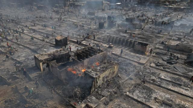 This aerial view shows people trying to salvage items from the burned down secondhand clothing market at Kantamanto in Accra, Ghana, on January 2, 2025. The fire at the Kantamanto market began in the early morning hours, destroying a large part of the area and displacing thousands of traders. (Photo by Nipah Dennis / AFP)