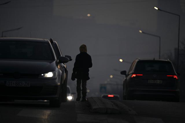 A young girl begs drivers for money in the thick smog of air pollution in Pristina, on January 2, 2025. (Photo by Armend NIMANI / AFP)