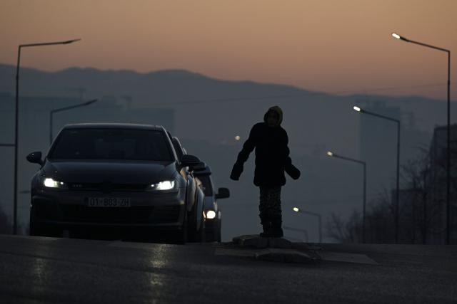 A young girl begs drivers for money in the thick smog of air pollution in Pristina, on January 2, 2025. (Photo by Armend NIMANI / AFP)