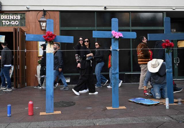 Tourists walk past as Eduardo Marquez paints crosses set up as a memorial near Bourbon Street on January 2, 2025 in New Orleans, Louisiana, the day after an attack by a man driving a truck down Bourbon street in the French Quarter. At least 15 people were killed and 30 injured on January 1 when a vehicle plowed overnight into a New Year's crowd in the heart of the thriving New Orleans tourist district, authorities in the southern US city said. (Photo by ANDREW CABALLERO-REYNOLDS / AFP)