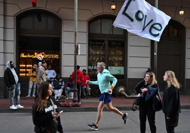 A man runs with a love flag down Bourbon Street on January 2, 2025 in New Orleans, Louisiana, the day after an attack by a man driving a truck down Bourbon street in the French Quarter. At least 15 people were killed and 30 injured on January 1 when a vehicle plowed overnight into a New Year's crowd in the heart of the thriving New Orleans tourist district, authorities in the southern US city said. (Photo by ANDREW CABALLERO-REYNOLDS / AFP)