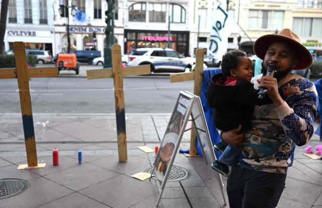 Amir ‘Tubad’ Gray sings holding his son near crosses set up as a memorial near Bourbon Street on January 2, 2025 in New Orleans, Louisiana, the day after an attack by a man driving a truck down Bourbon street in the French Quarter. At least 15 people were killed and 30 injured on January 1 when a vehicle plowed overnight into a New Year's crowd in the heart of the thriving New Orleans tourist district, authorities in the southern US city said. (Photo by ANDREW CABALLERO-REYNOLDS / AFP)