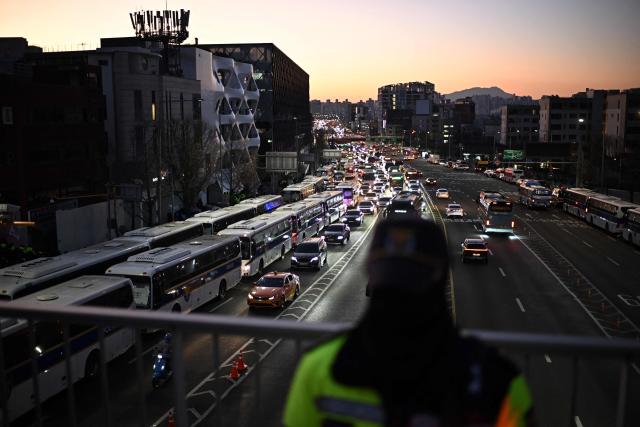 South Korean police vehicles (L) gather near the residence of South Korea's impeached President Yoon Suk Yeol in Seoul on January 3, 2025. South Korea's impeached President Yoon Suk Yeol remained defiantly in his residence in Seoul on Thursday as investigators probing his ill-fated declaration of martial law sought to detain him for questioning. Investigators have an arrest warrant but Yoon's die-hard supporters, including far-right YouTube personalities, are gathering outside in a bid to protect him, setting up potential clashes with police and anti-Yoon protesters. (Photo by Philip FONG / AFP)