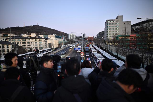 Members of the media stand on the footbridge near the residence of South Korea's impeached President Yoon Suk Yeol as police vehicles gather in Seoul on January 3, 2025. South Korea's impeached President Yoon Suk Yeol remained defiantly in his residence in Seoul on Thursday as investigators probing his ill-fated declaration of martial law sought to detain him for questioning. Investigators have an arrest warrant but Yoon's die-hard supporters, including far-right YouTube personalities, are gathering outside in a bid to protect him, setting up potential clashes with police and anti-Yoon protesters. (Photo by Philip FONG / AFP)