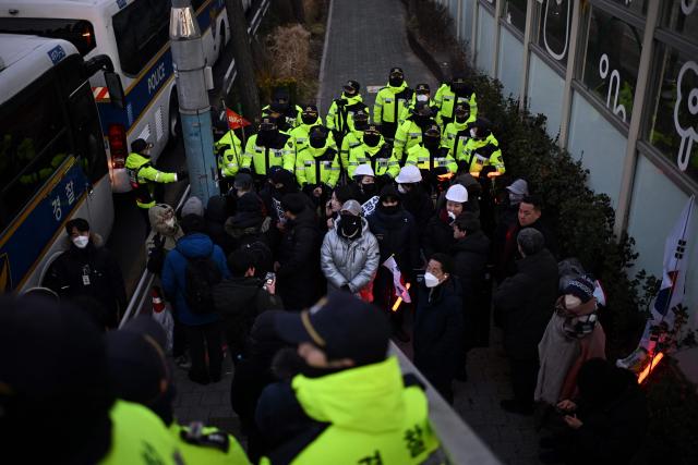 Members of the media stand on the footbridge near the residence of South Korea's impeached President Yoon Suk Yeol as police vehicles gather in Seoul on January 3, 2025. South Korea's impeached President Yoon Suk Yeol remained defiantly in his residence in Seoul on Thursday as investigators probing his ill-fated declaration of martial law sought to detain him for questioning. Investigators have an arrest warrant but Yoon's die-hard supporters, including far-right YouTube personalities, are gathering outside in a bid to protect him, setting up potential clashes with police and anti-Yoon protesters. (Photo by Philip FONG / AFP)